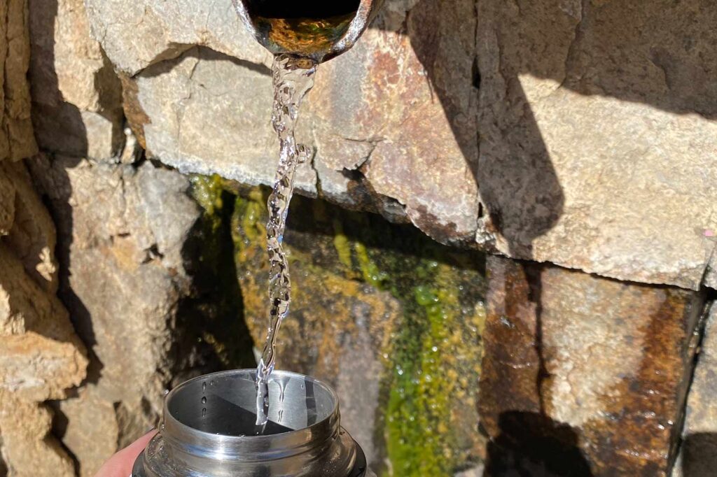 spring water coming out of a pipe in a rock wall filling a water bottle