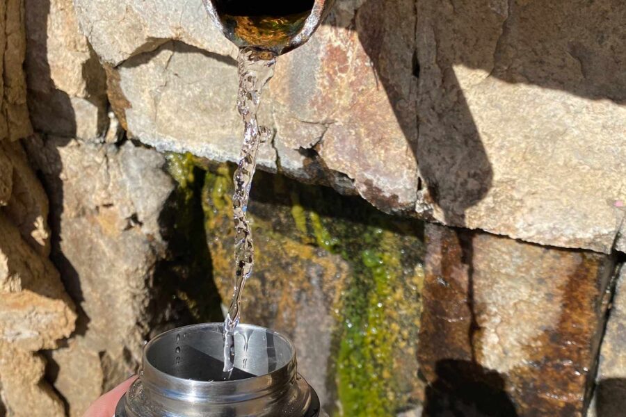spring water coming out of a pipe in a rock wall filling a water bottle